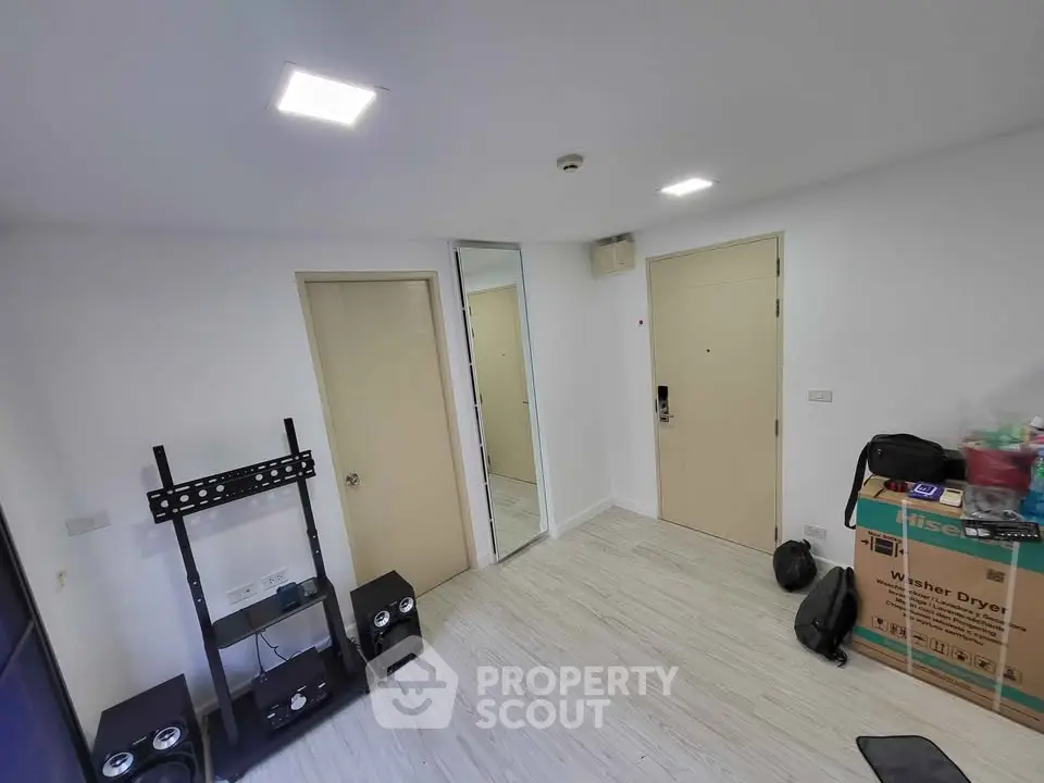 Modern apartment interior with light wood flooring and minimalistic decor, featuring a washer dryer box and speaker setup.
