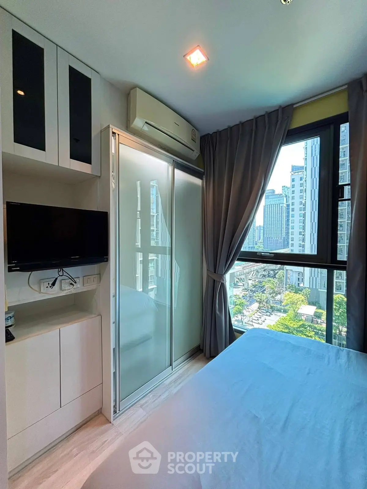 Modern bedroom with city view, featuring sleek built-in storage and a wall-mounted TV.