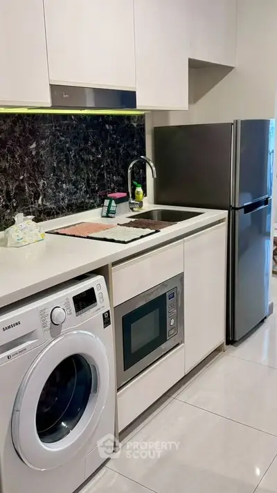 Modern kitchen with sleek appliances including washing machine, microwave, and fridge in compact layout.