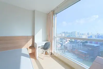 Bright bedroom with city view, featuring a desk and large window.