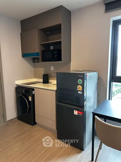 Modern compact kitchen with fridge, washing machine, and microwave in a cozy apartment.