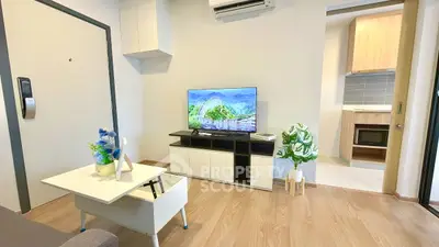 Modern living room with stylish decor and open kitchen layout, featuring a sleek TV setup and wooden flooring.