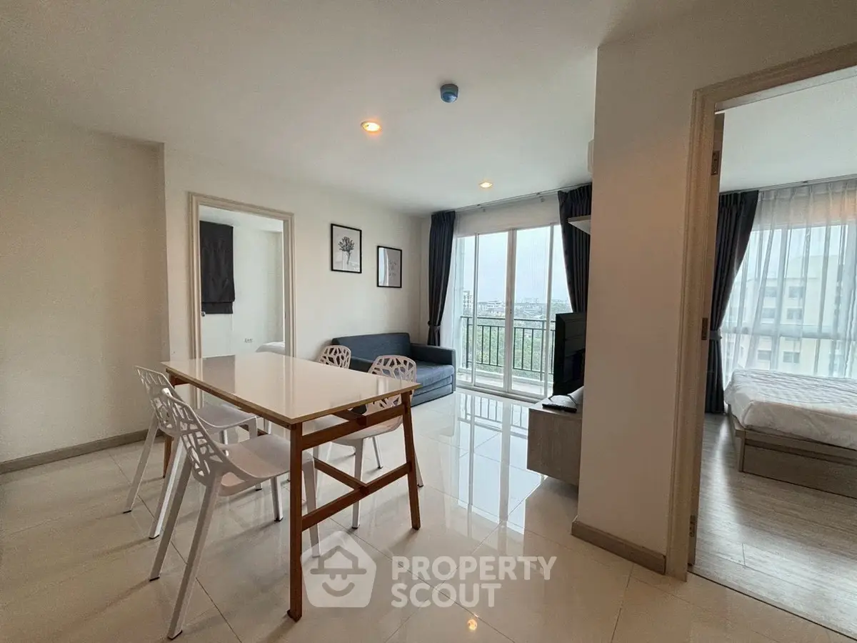 Modern apartment interior with dining area and living room, featuring large windows and natural light.