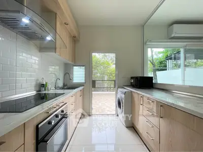 Modern kitchen with sleek cabinetry, built-in oven, and washing machine, overlooking a lush outdoor view.