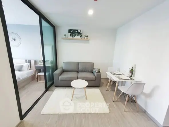 Modern living room with gray sofa, white rug, and dining area in open layout apartment.