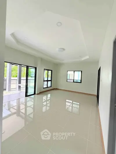 Spacious modern living room with large windows and glossy tiled floors, offering abundant natural light.