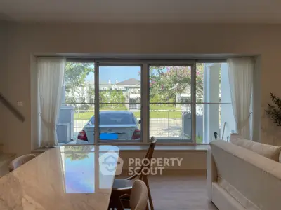 Spacious living room with large window offering serene garden view and elegant dining area.