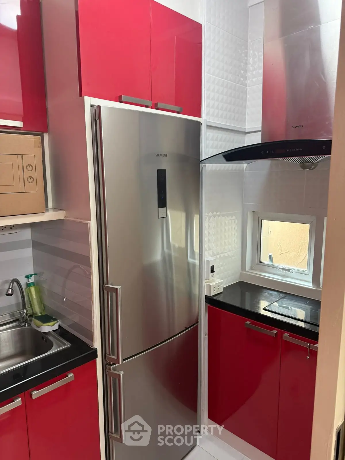Modern kitchen with red cabinets and stainless steel appliances, featuring a sleek fridge and compact design.