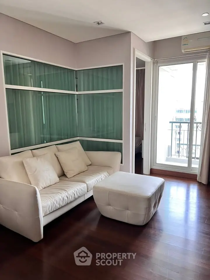 Modern living room with white sofa, ottoman, and balcony access in a stylish apartment.