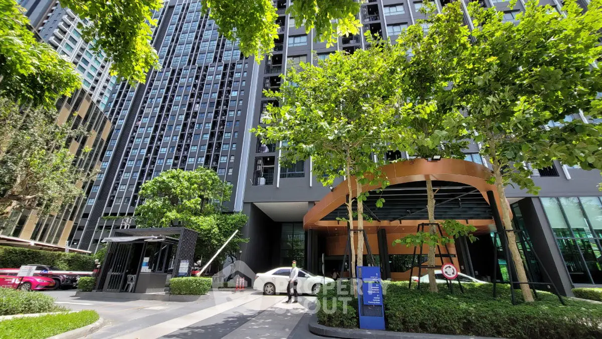 Modern high-rise building entrance with lush greenery and sleek design.