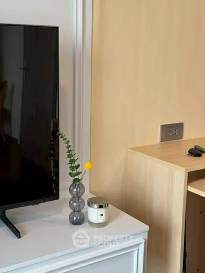 Modern living room corner with TV, stylish vase, and candle on a sleek cabinet.