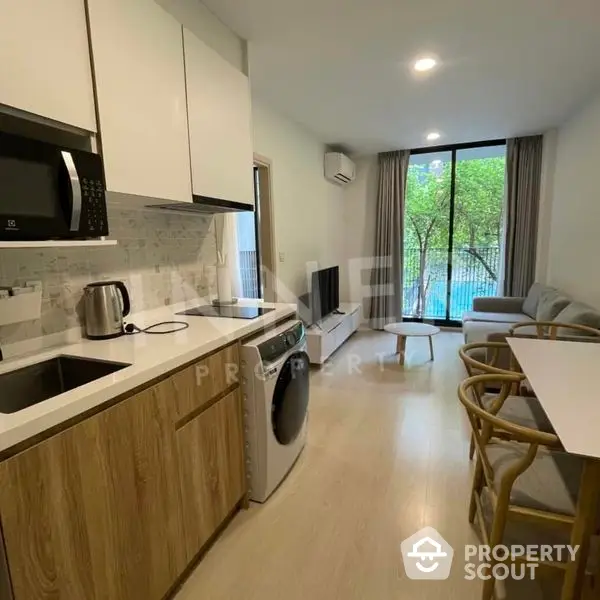 Modern studio apartment with a sleek kitchen featuring stainless steel appliances, ample cabinetry, and a cozy living area with natural light and balcony access.