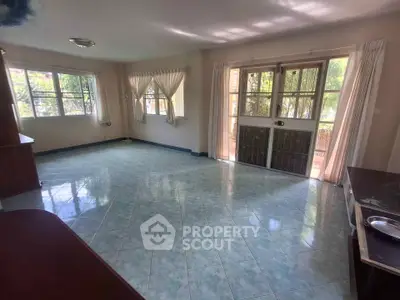 Spacious living room with large windows and tiled flooring, offering abundant natural light.