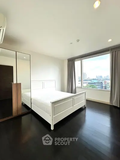 Modern bedroom with large window offering city view and sleek dark flooring.