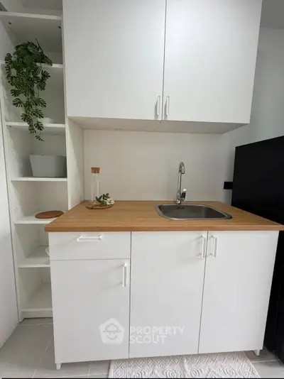 Modern compact kitchen with sleek white cabinets and wooden countertop, perfect for small spaces.