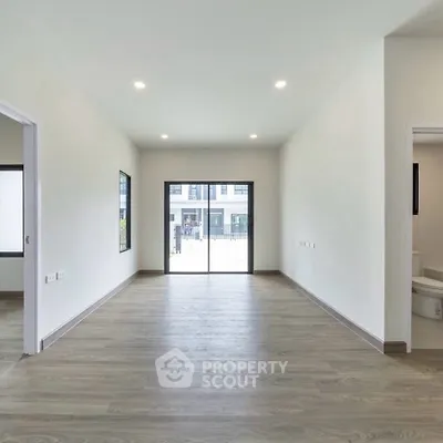 Spacious empty room with wooden flooring and large window, ideal for customization.