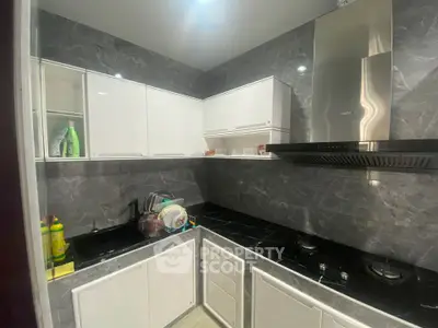 Modern kitchen with sleek white cabinets and black countertops, featuring a gas stove and stainless steel range hood.