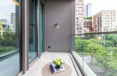 Modern balcony with glass railing offering cityscape views and lush greenery, perfect for relaxation.