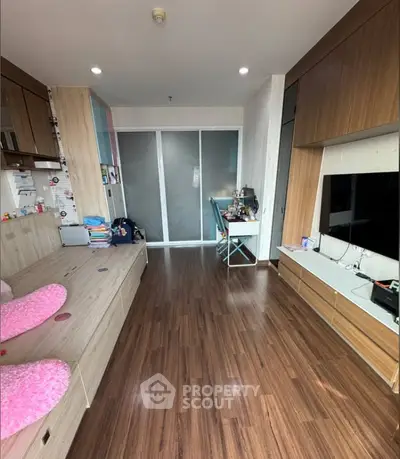 Modern living room with wooden flooring and built-in storage, featuring a cozy workspace and entertainment area.