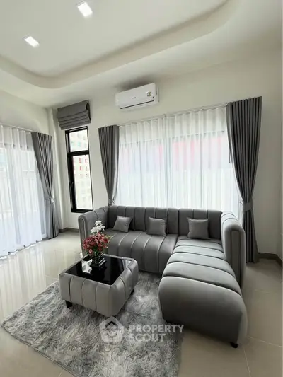 Modern living room with sleek gray sofa, plush rug, and large windows for natural light.