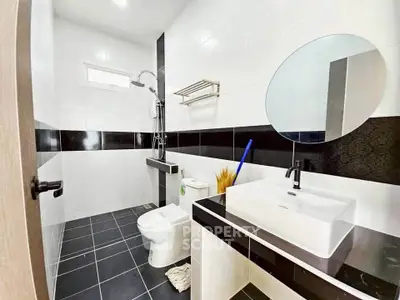 Modern bathroom with sleek black and white tiles, round mirror, and contemporary fixtures.