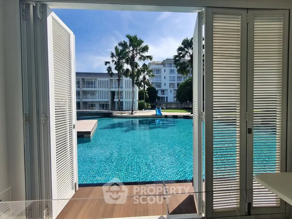 Luxurious poolside view from modern apartment with open shutters and palm trees.