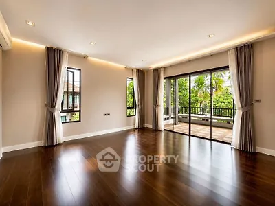 Spacious living room with hardwood floors and large windows opening to a lush balcony view.