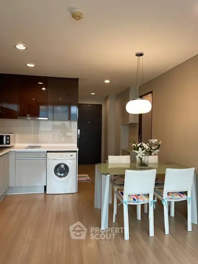 Modern kitchen with dining area, featuring washing machine and stylish lighting.