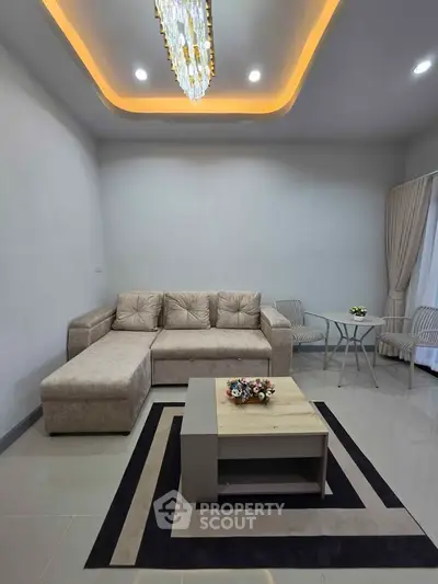 Modern living room with elegant chandelier, beige sectional sofa, and stylish coffee table.