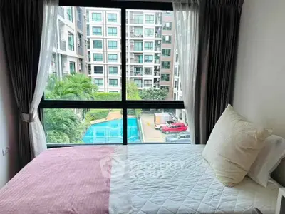 Cozy bedroom with large window offering pool and garden view in modern apartment complex.