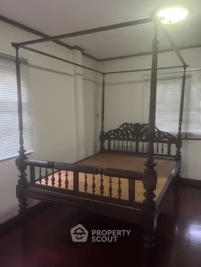 Elegant bedroom featuring a vintage four-poster bed, polished wooden floors, and ample natural light from large windows with blinds.
