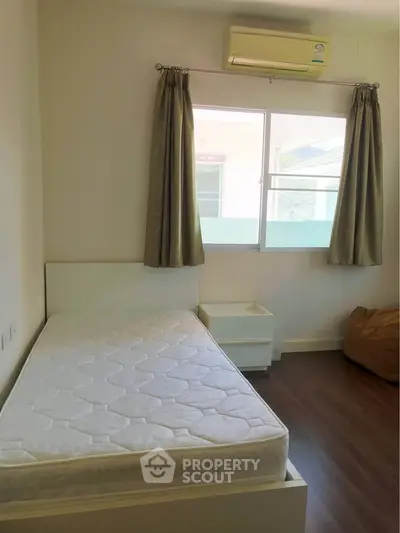 Cozy bedroom with natural light and air conditioning, featuring a single bed and hardwood floors.