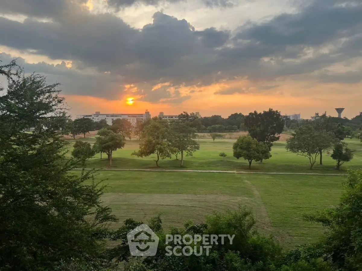 Stunning sunset view over lush green golf course with trees and distant buildings.
