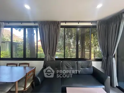 Spacious living room with large windows and garden view, featuring modern furniture and elegant curtains.