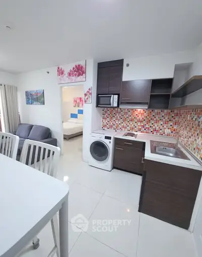 Modern open-plan kitchen with colorful backsplash and washing machine in a cozy apartment.