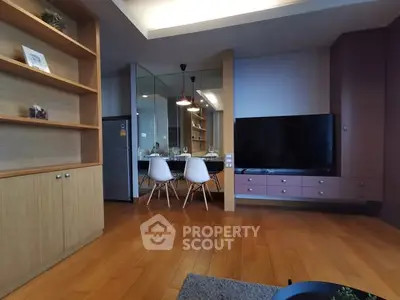 Modern living room with wooden flooring and large TV, open dining area with stylish chairs.