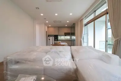 Spacious modern living room with large windows and open kitchen layout, featuring new furniture.