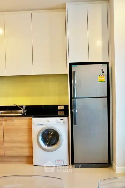 Modern kitchen with sleek cabinets, washing machine, and stainless steel fridge.