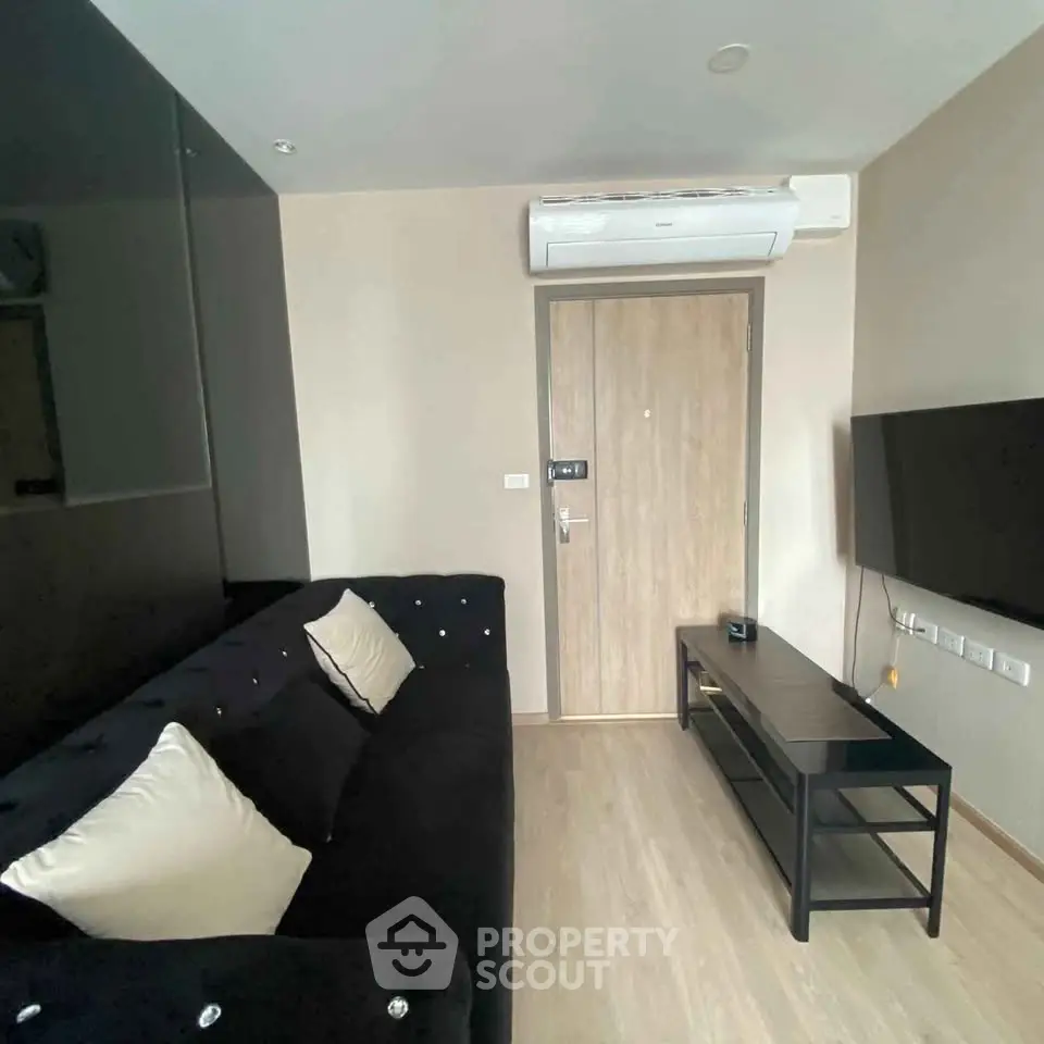 Modern living room with sleek black sofa, wall-mounted TV, and air conditioning unit.