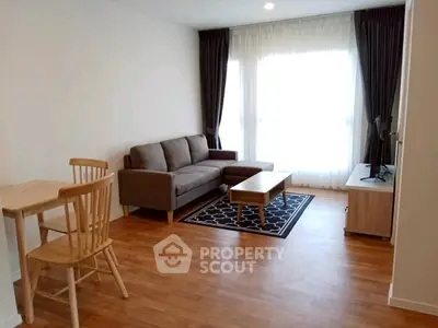 Modern living room with wooden flooring, cozy sofa, and natural light from large windows.