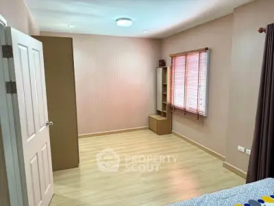 Spacious bedroom with wooden flooring and ample natural light from window blinds.