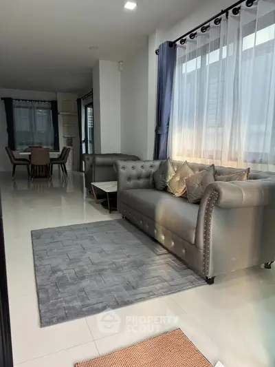 Elegant living room with plush sofa and dining area, featuring large windows and modern decor.