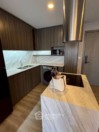 Modern kitchen with sleek wooden cabinets and marble countertops, featuring built-in appliances and a washing machine.