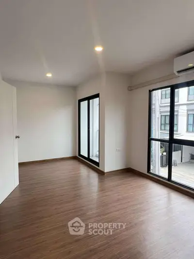 Spacious empty room with wooden flooring and large windows offering natural light.