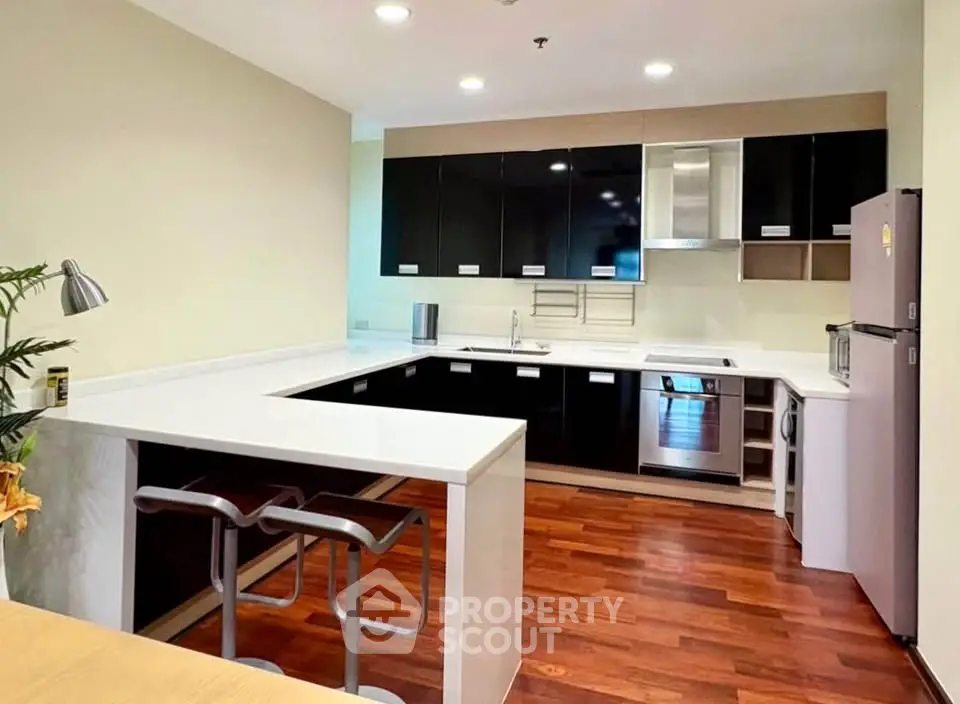 Modern kitchen with sleek black cabinets and hardwood floors, featuring a breakfast bar and stainless steel appliances.