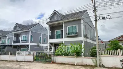 Modern two-story gray house with balcony and gated front yard in suburban neighborhood.