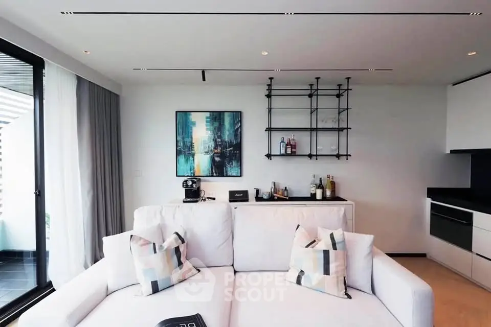 Modern living room with stylish decor and open kitchen layout, featuring a cozy sofa and elegant shelving.