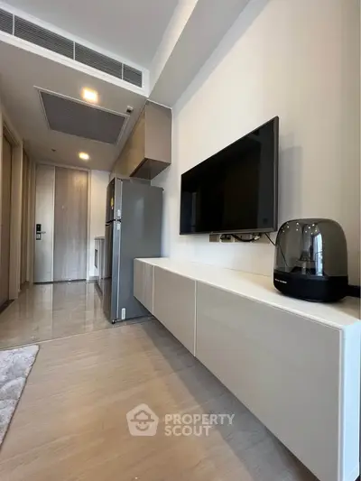 Modern apartment interior with sleek kitchen and stylish living area, featuring a wall-mounted TV and contemporary decor.