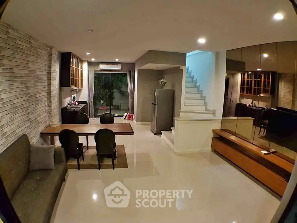 Modern open-plan living room with dining area and staircase, featuring stylish decor and ample natural light.