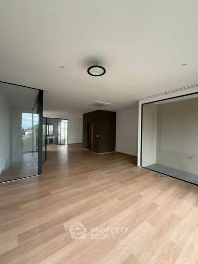 Spacious modern living room with wooden flooring and glass partitions.